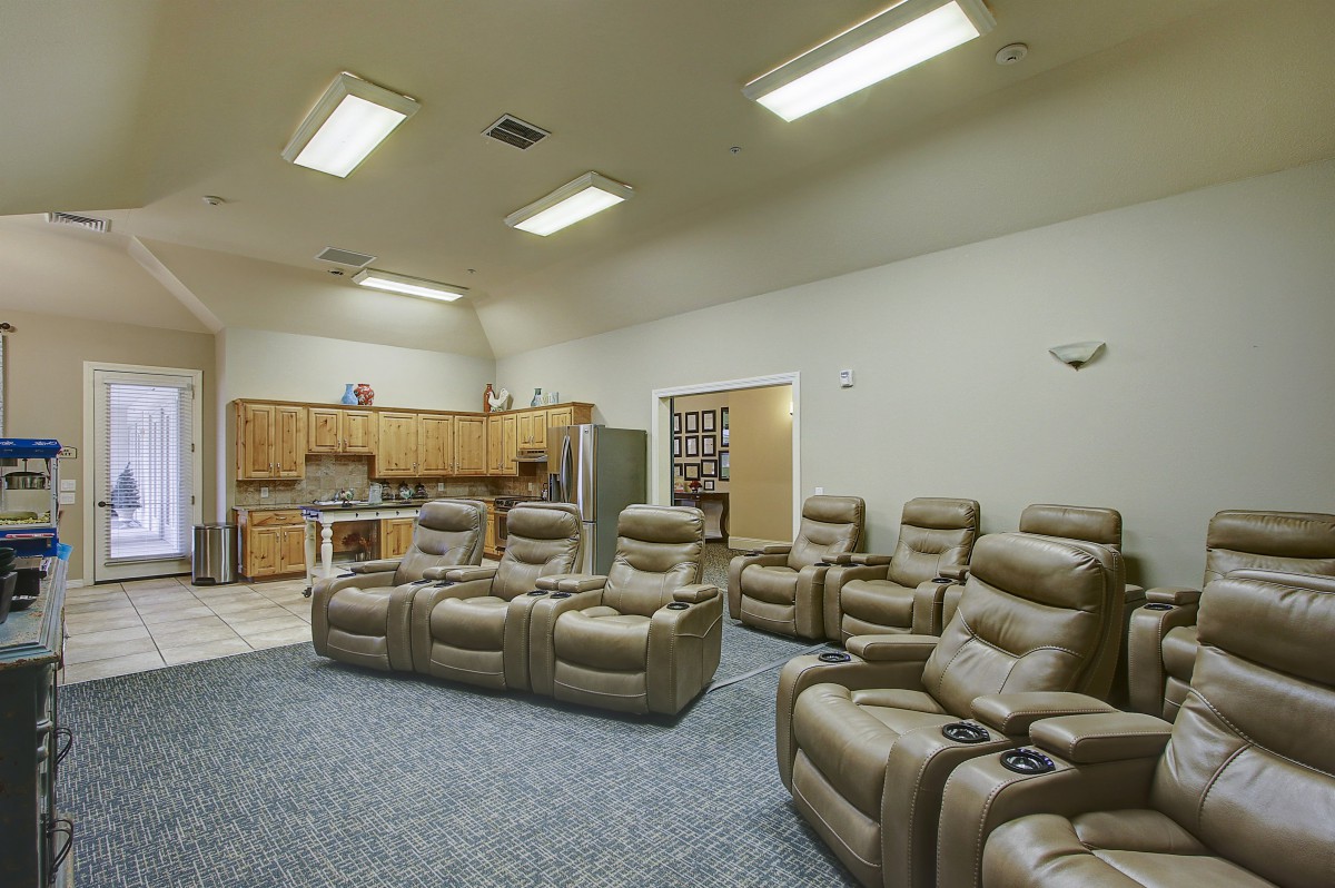 A cozy home theater setup with multiple recliner chairs and an adjoining kitchen area.