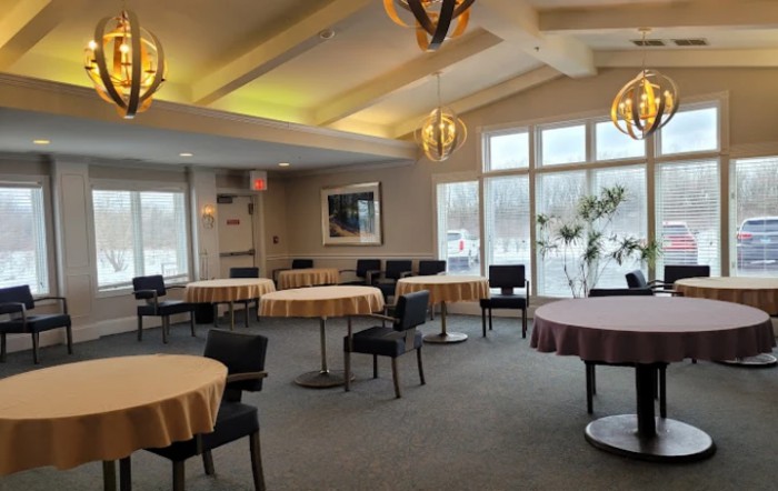 An empty restaurant dining area with neatly arranged tables and chairs, featuring large windows and modern lighting.