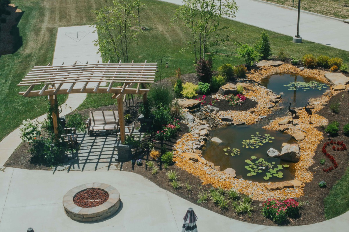 A beautifully landscaped garden featuring a pond, pergola, and fire pit area.
