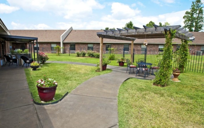 A garden with a pathway and outdoor seating under a pergola, set in front of a building.