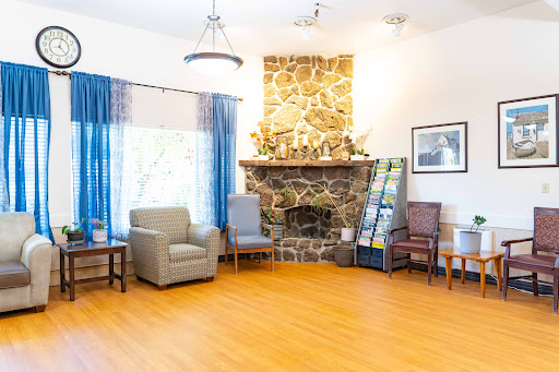 A cozy and inviting living room with a stone fireplace, comfortable chairs, and plenty of natural light.