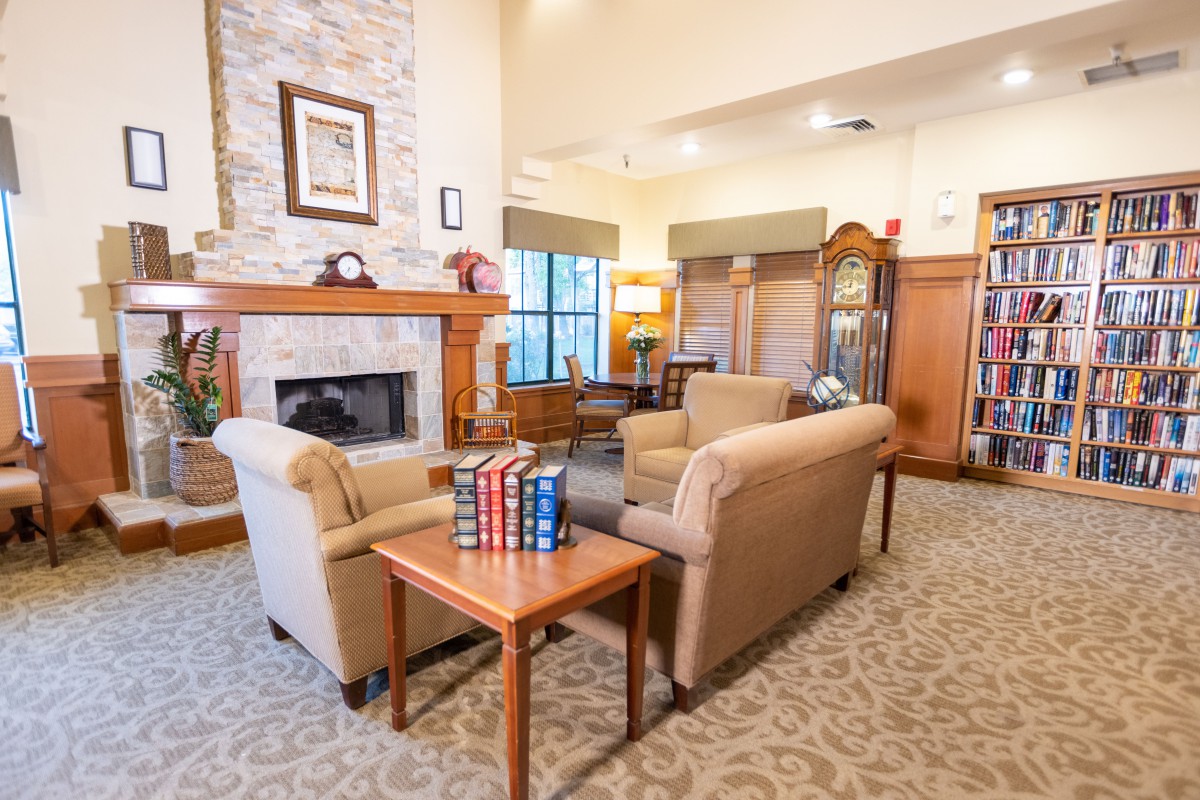 A cozy living room with a fireplace and armchairs, decorated with books and a grandfather clock.