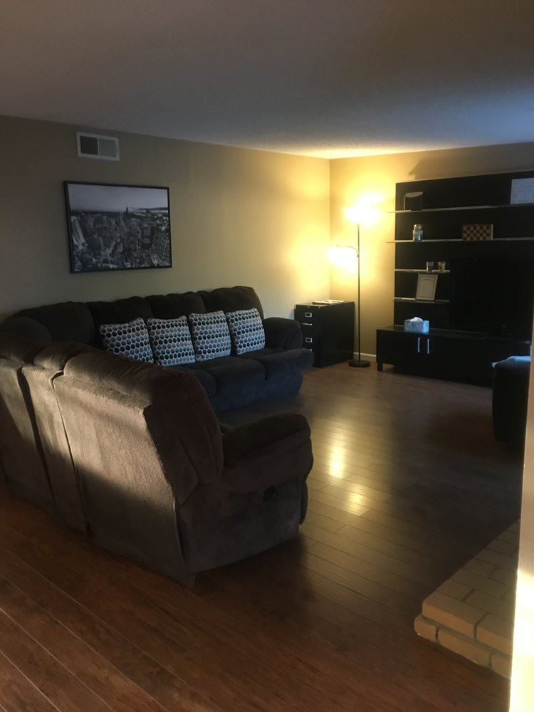 A cozy living room with a sofa, lamp, and shelving unit on a wooden floor.