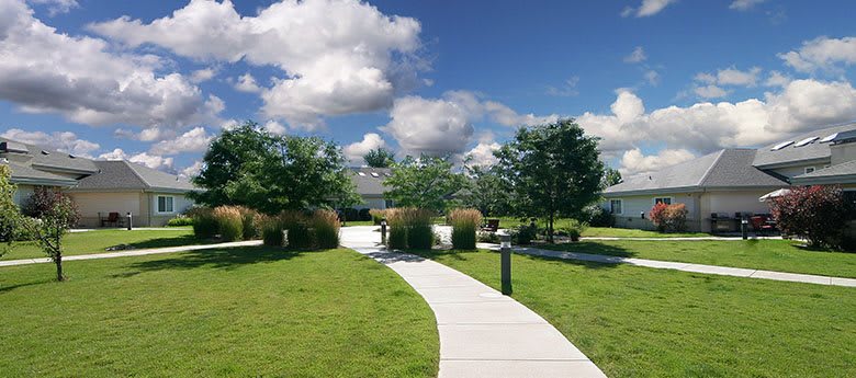 A scenic garden path surrounded by lush green grass and trees under a partly cloudy sky.