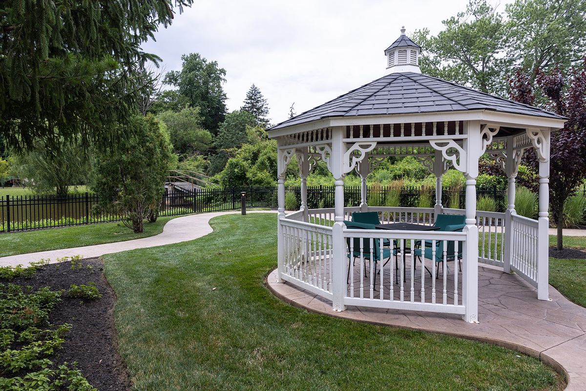 A scenic garden featuring a white gazebo and winding pathway surrounded by lush greenery.