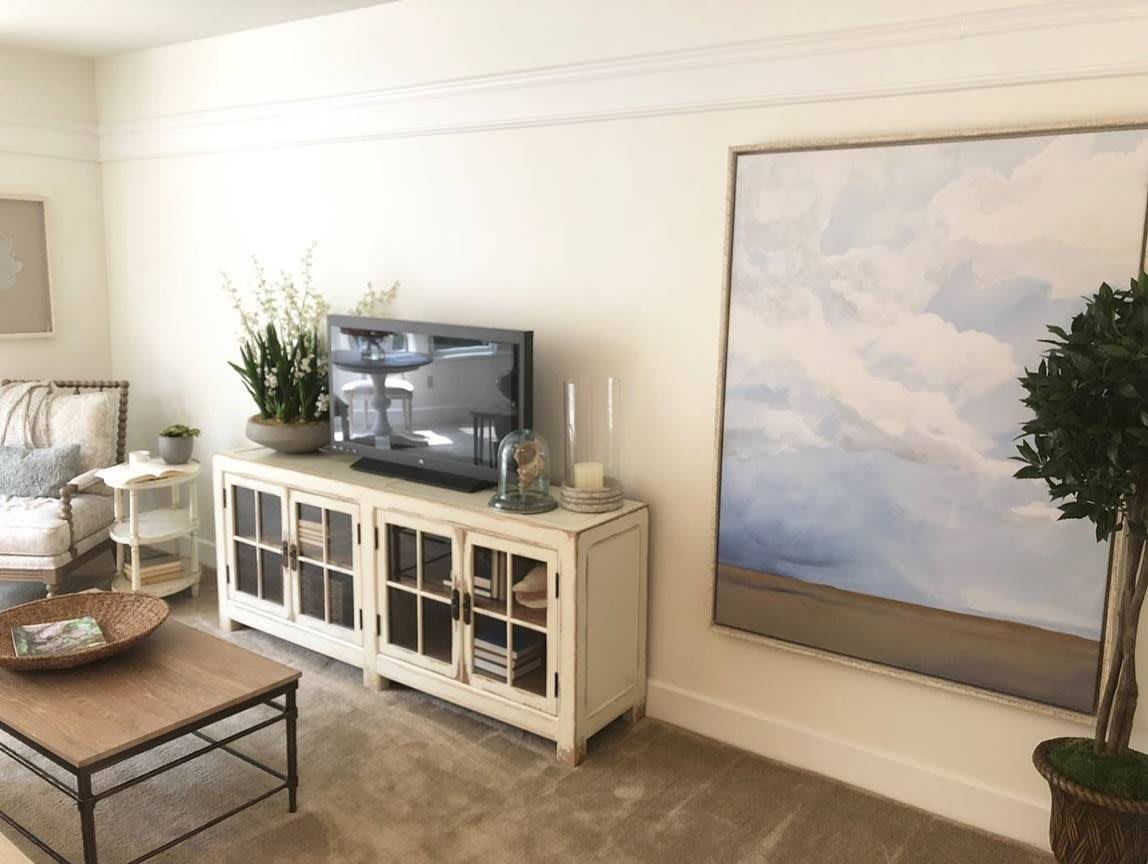A cozy living room with a TV, decorative plants, and large framed artwork.