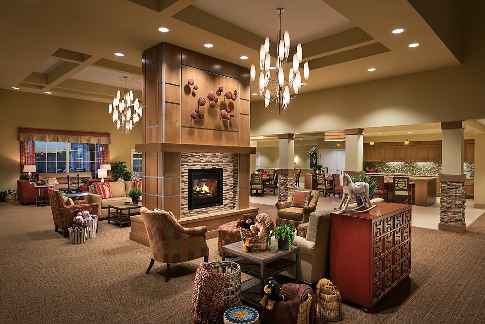 A cozy living room with a central fireplace, surrounded by comfortable furniture and illuminated by elegant chandeliers.