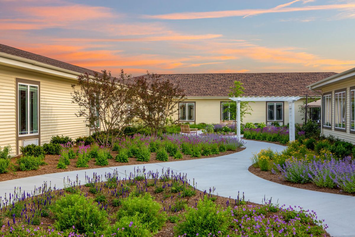 A beautiful garden path leads to a cozy house under a colorful sunset sky.
