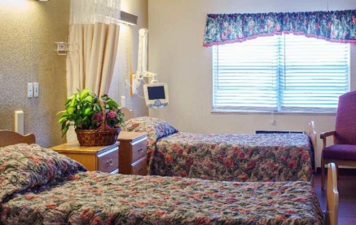 A hospital room featuring two beds and a monitor, decorated with floral curtains and a basket of flowers.