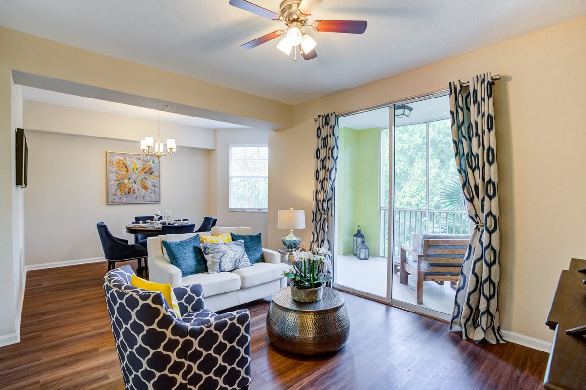 A well-lit living room with a dining area, featuring a wooden floor, modern furniture, and access to a balcony.