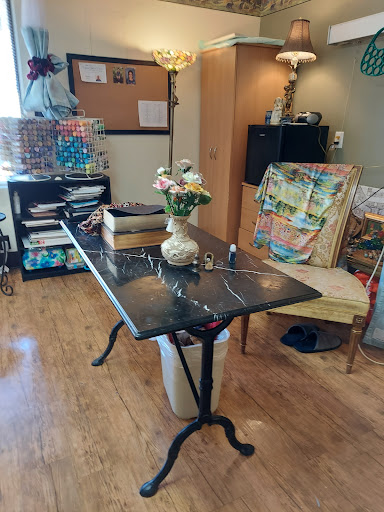 A cozy workspace featuring a table with a flower vase and a chair, alongside shelves filled with books and materials.