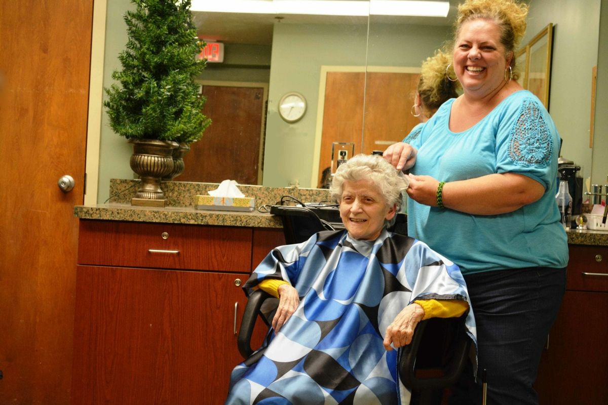 An older woman getting a haircut by a smiling hairstylist in a salon.