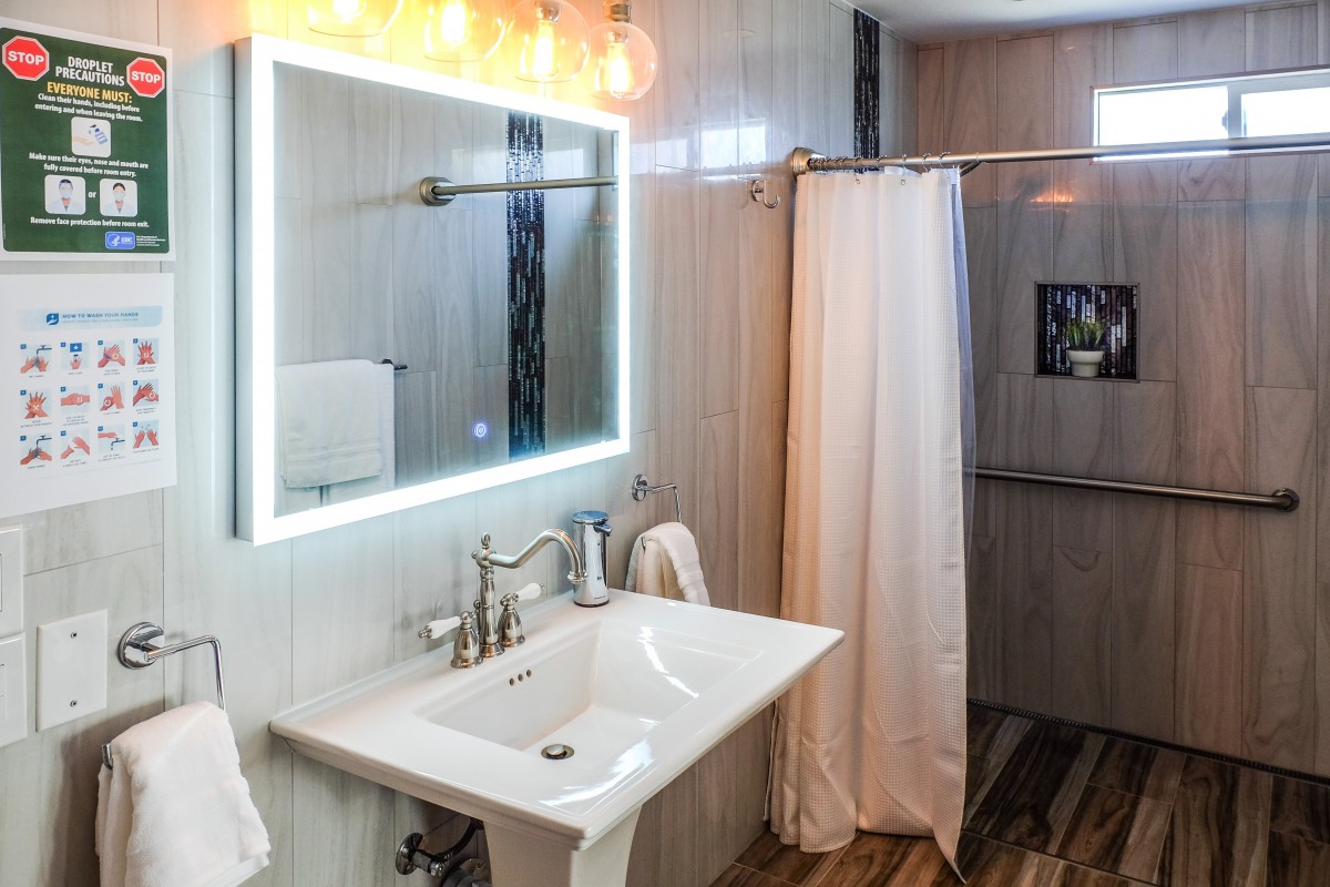 A modern bathroom with a well-lit mirror, sink, and shower area.