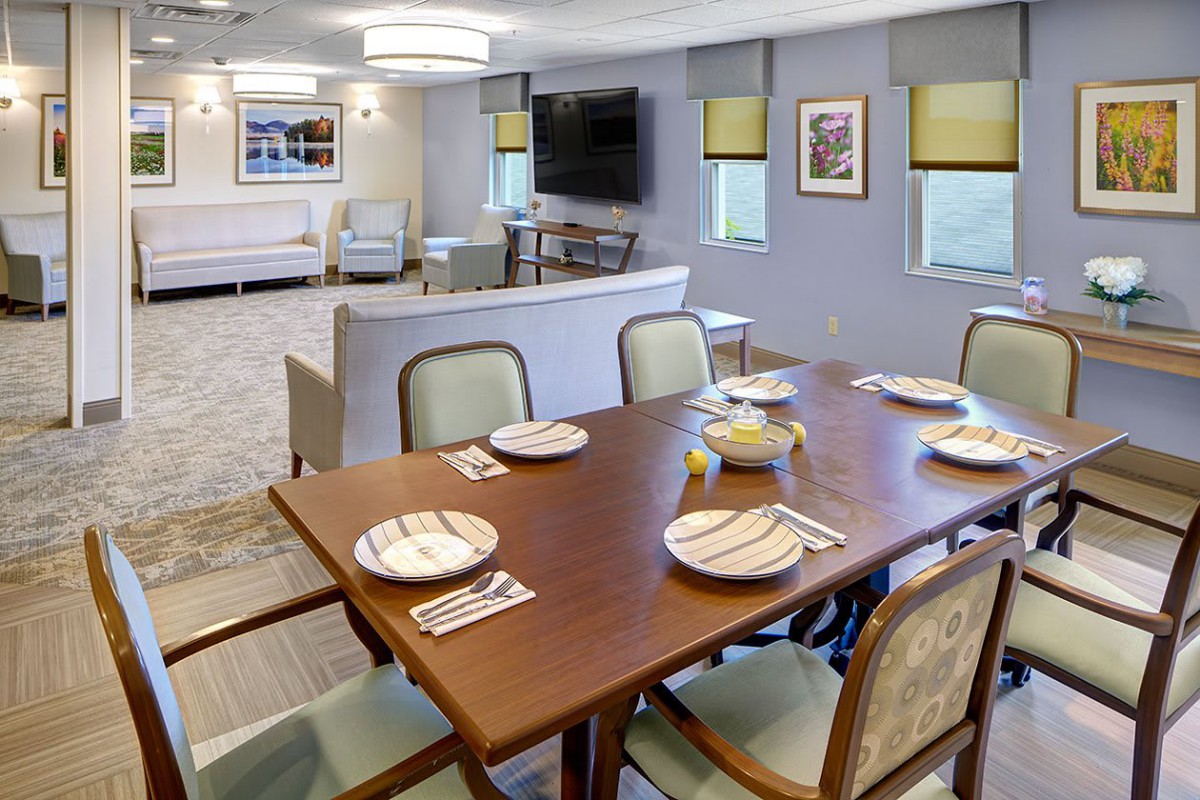 A cozy dining room setup with a table set for six, adjacent to a comfortable living area with a television.