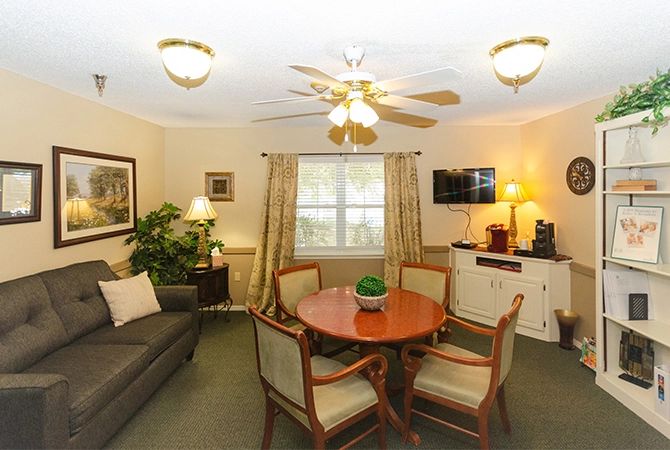 A cozy living room with a round table, chairs, a sofa, and a ceiling fan.