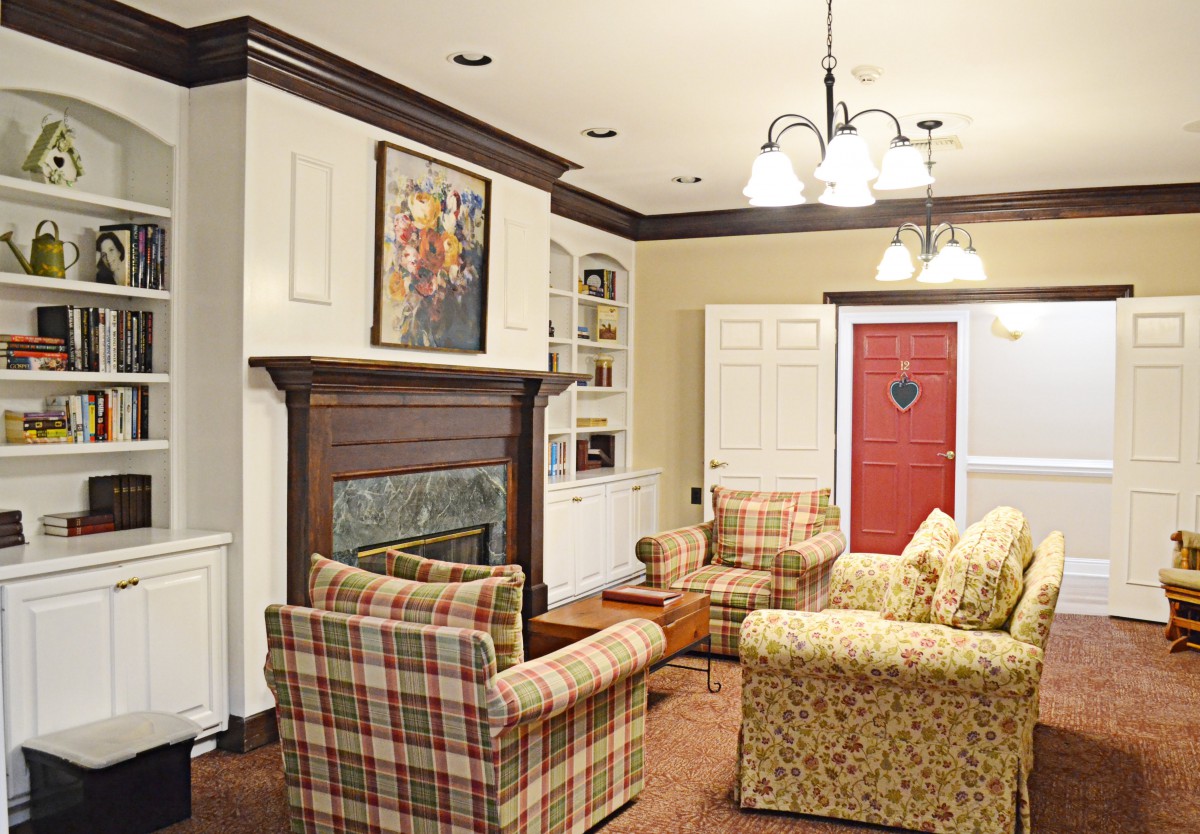 A cozy living room with a fireplace, plaid chairs, and a red door.