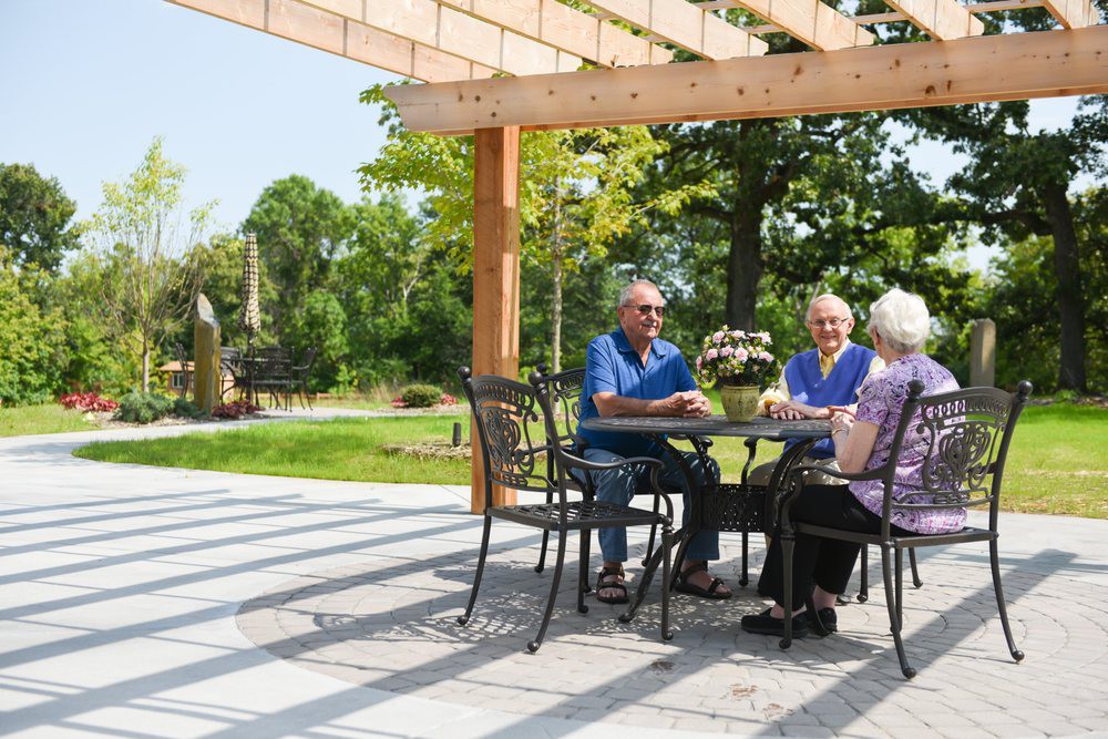 A group of seniors enjoying a conversation under a pergola in a garden setting.