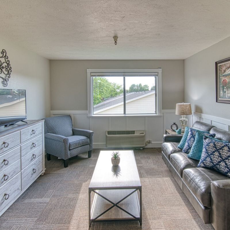 A cozy living room with a sofa, armchair, and coffee table, featuring a window with a view.