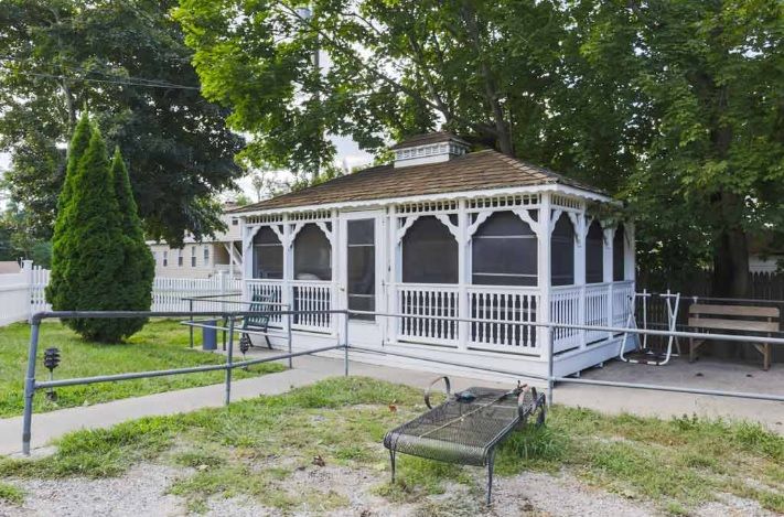 A white gazebo surrounded by trees with a bench in the foreground.