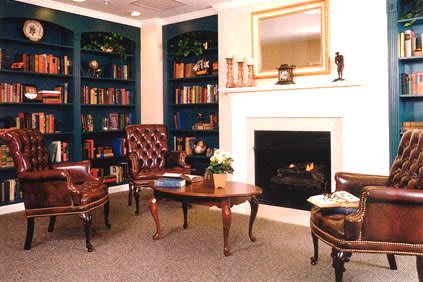 A cozy library interior with bookshelves, a fireplace, and comfortable seating.