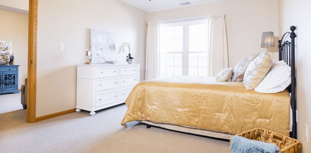 A bright, well-lit bedroom featuring a gold bedspread and white furniture.