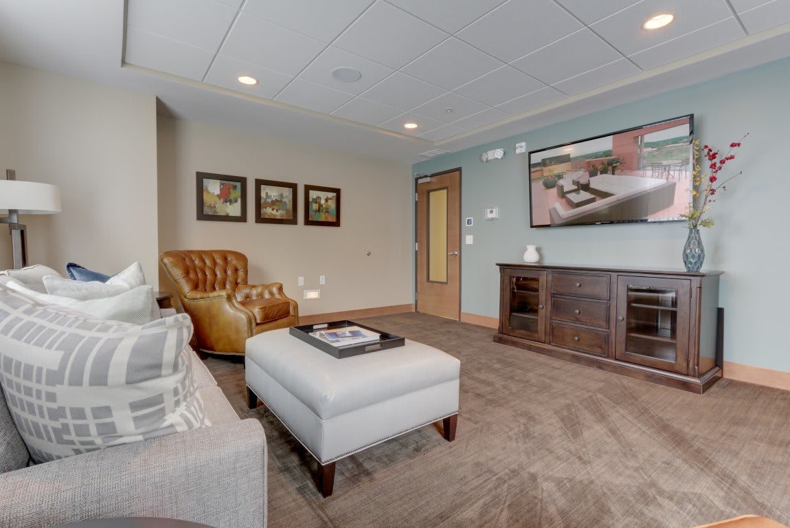 A cozy living room with a sofa, leather chair, ottoman, and a television stand.