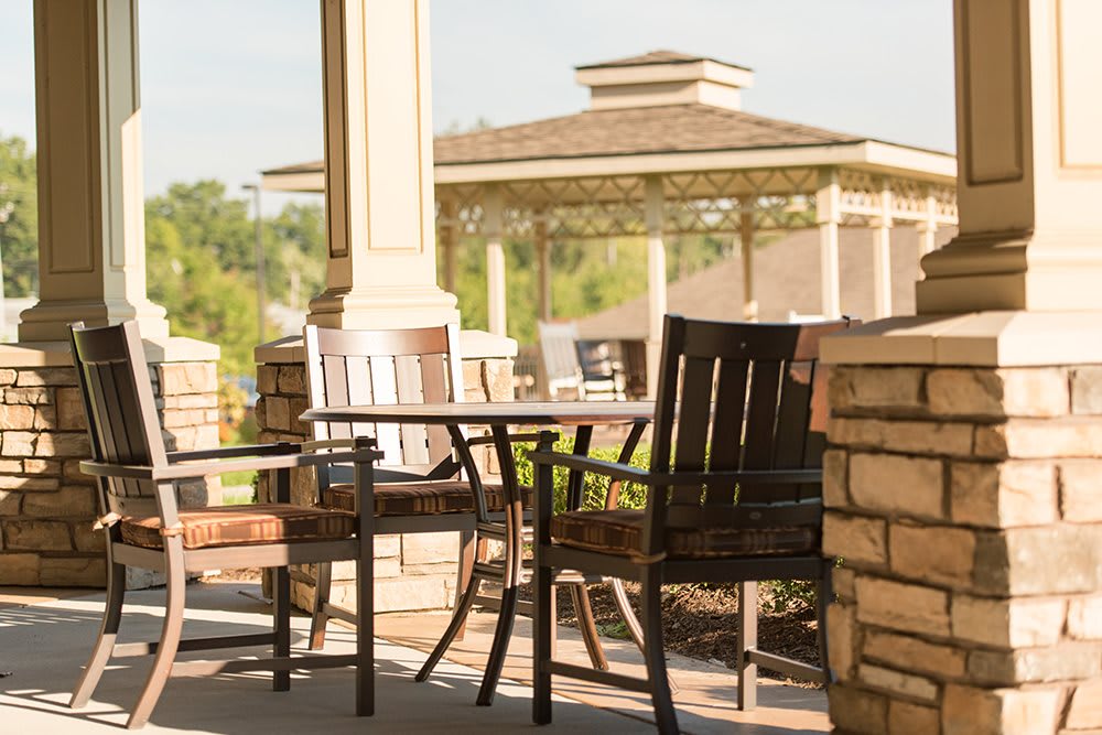 A sunny patio with wooden chairs and a table, overlooking a gazebo.