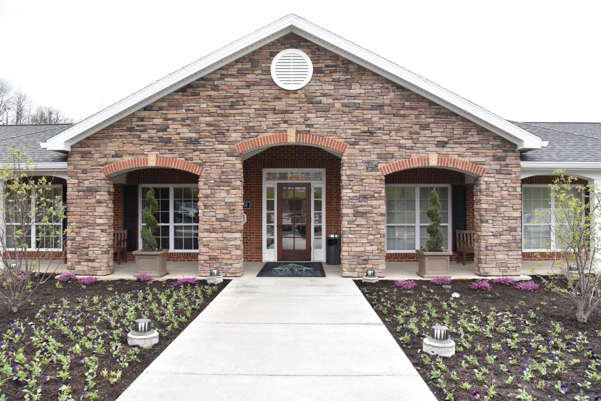 A brick house with a symmetrical entrance, featuring two windows and a landscaped walkway.