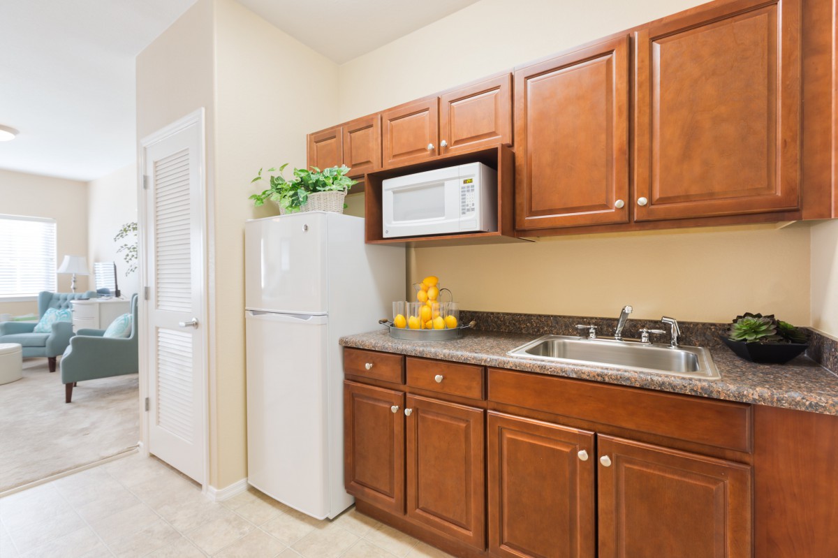 A modern kitchen featuring wooden cabinets, a refrigerator, microwave, and sink.