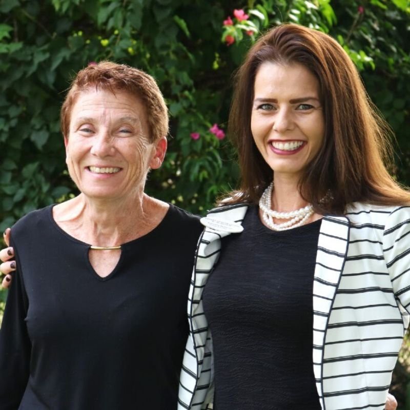 Two women smiling outdoors in a garden setting.