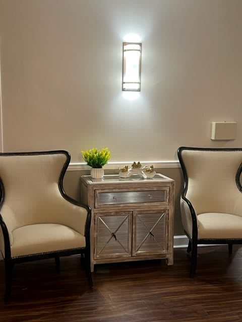 A cozy seating area with two elegant chairs and a decorative table, softly lit by a wall sconce.