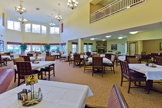 A spacious dining area with multiple tables and chairs, featuring bright lighting and large windows.