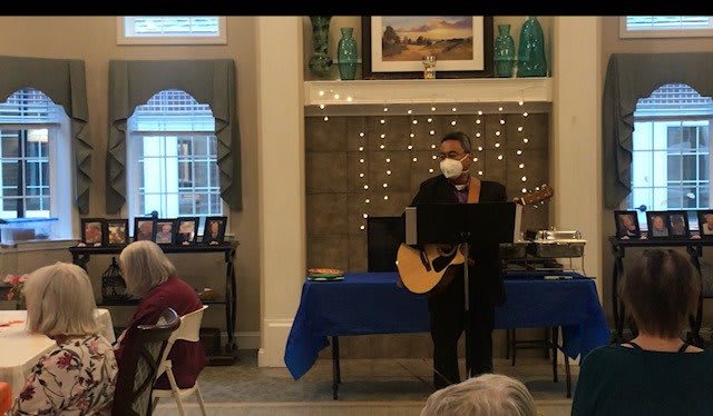 A musician performs indoors, playing guitar and singing to an audience.