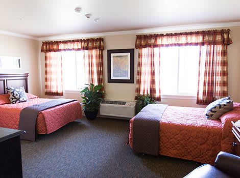 A hotel room with two beds, large windows, and elegant decor.