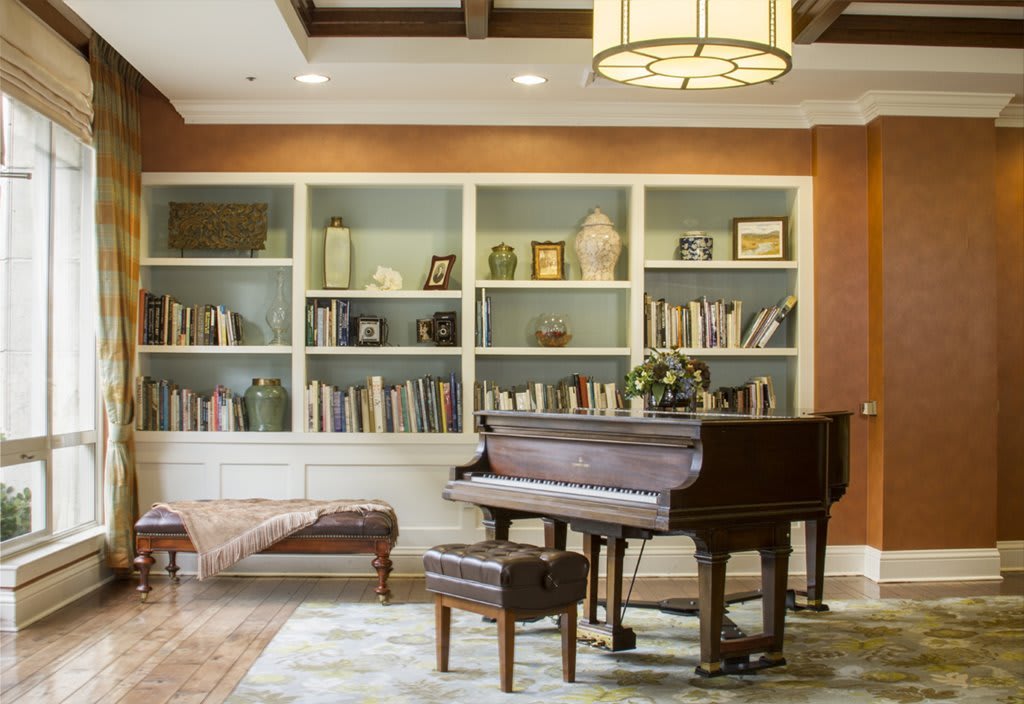 A cozy living room featuring a grand piano and bookshelves filled with books.