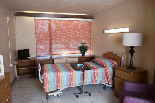 A well-lit hospital patient room featuring a single bed, desk, and a window adorned with patterned blinds.