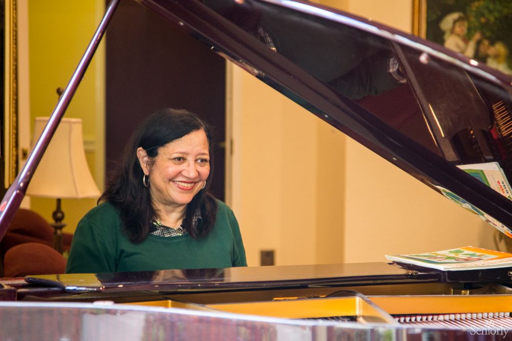 A woman smiling while sitting at a piano indoors.