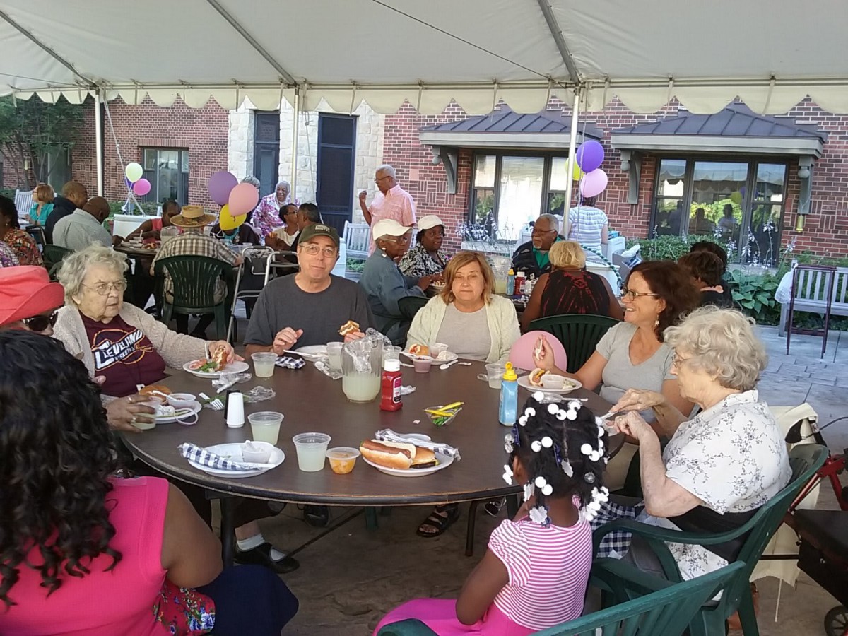 A group of people enjoying a meal together under a tent, with balloons in the background.