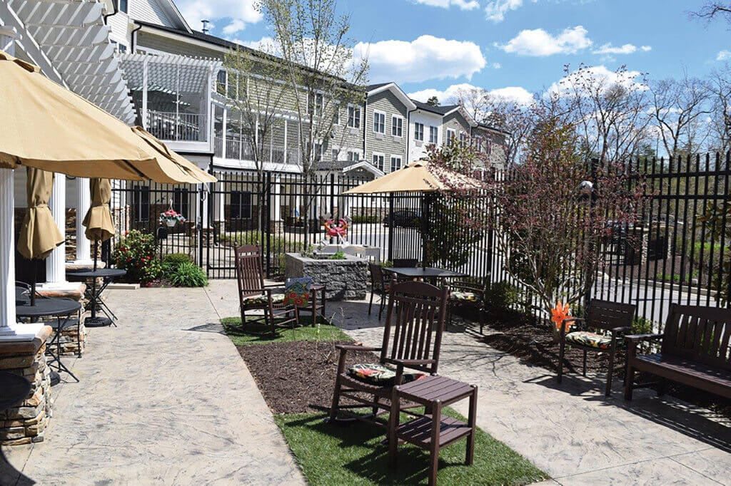 A peaceful outdoor patio area with chairs and umbrellas, surrounded by garden landscaping and adjacent buildings.