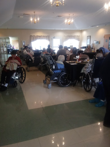 A bustling common area in an assisted living facility, featuring elderly residents socializing and relaxing in wheelchairs.