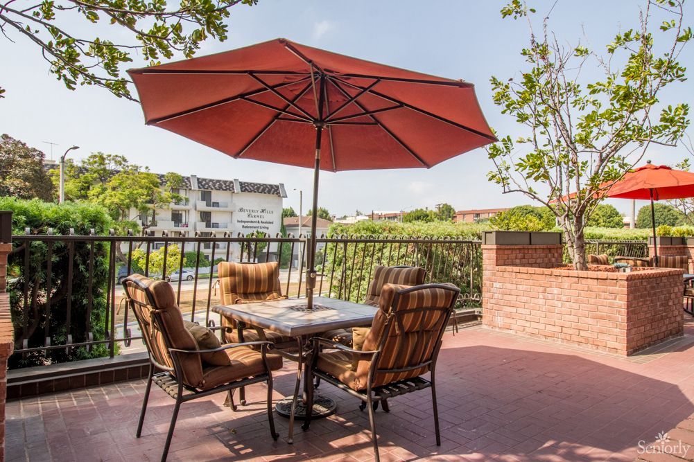 A sunny patio with outdoor furniture and an umbrella, overlooking greenery.