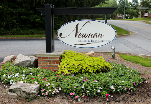 Entrance sign for Newman Health & Resort surrounded by blooming flowers and lush plants.