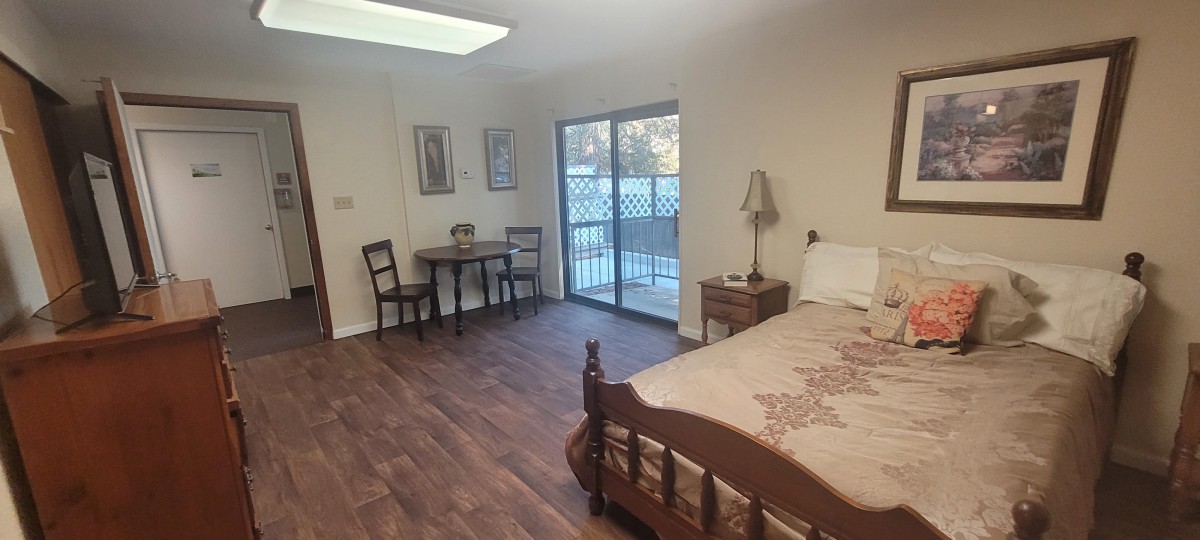 A cozy bedroom with a wooden bed, small table and chairs, and a sliding glass door.