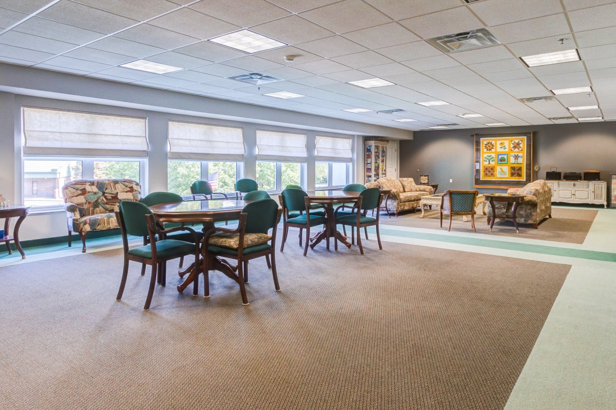 A spacious and well-lit room featuring multiple tables and chairs, with large windows allowing natural light to fill the space.