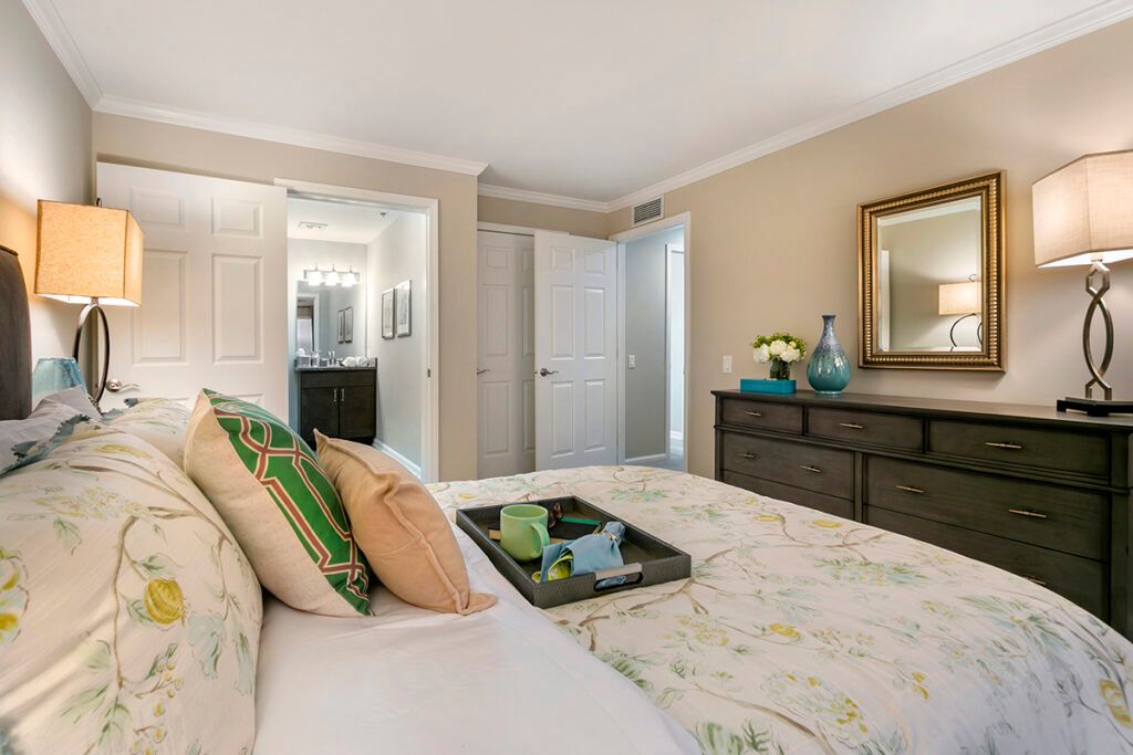 A cozy bedroom featuring a neatly made bed with decorative pillows and a tray, complemented by a dresser with a mirror on the wall.