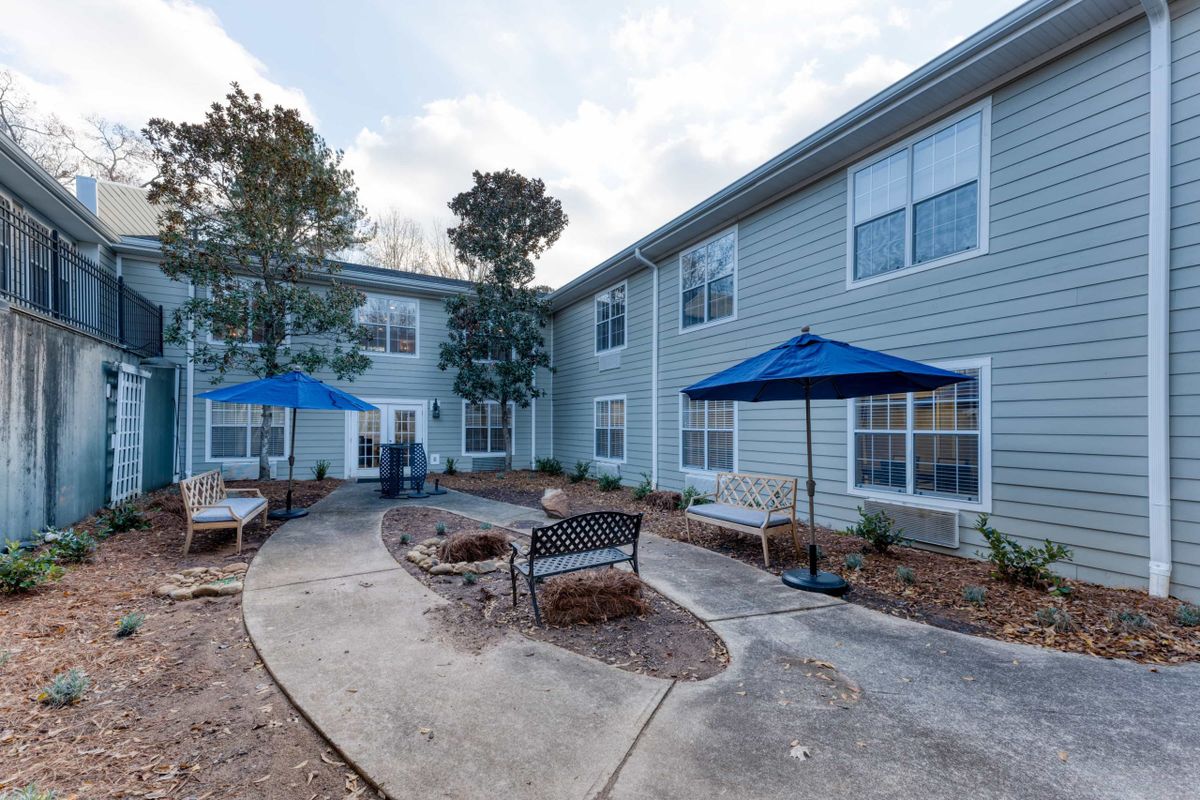A serene outdoor courtyard with benches and blue umbrellas next to a residential building.