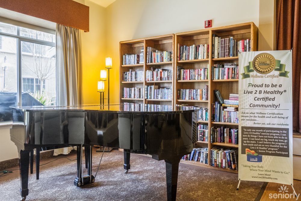 A grand piano in a cozy library setting with filled bookshelves.