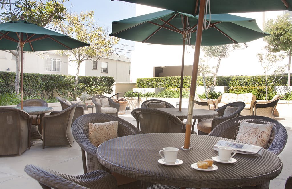 A cozy outdoor patio with rattan chairs and tables, featuring coffee cups under large umbrellas on a sunny day.