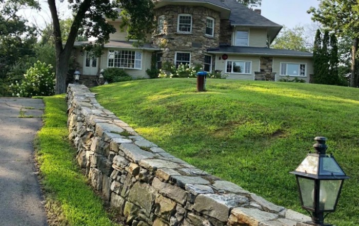 A large stone house with a surrounding stone wall and well-maintained lawn.