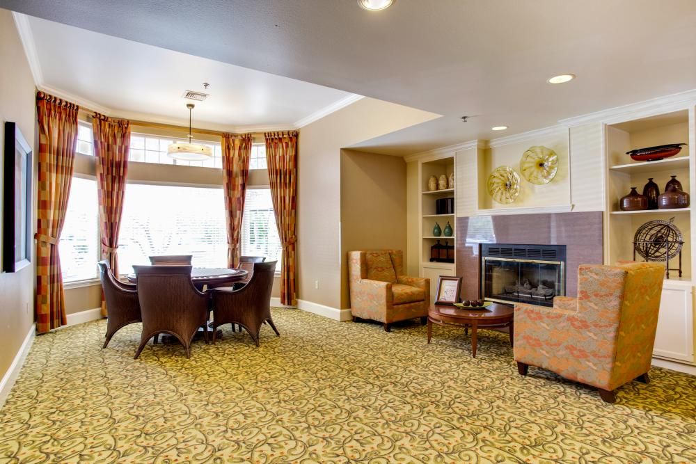 A cozy living room with a fireplace, comfortable chairs, and a dining table near large windows.